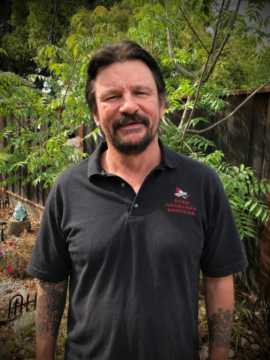 Richard, owner of RC&G Handyman Services, standing in his backyard wearing the company polo shirt.